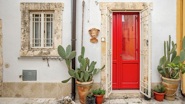 A building with a red door, a window with bars, and several potted cacti. - Casa Keller con Terrazza by Wonderful Italy (Noto)