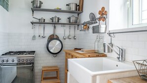 A modern kitchen with a gas stove, white sink, wooden stool, and hanging utensils. - Casa Keller con Terrazza by Wonderful Italy (Noto)