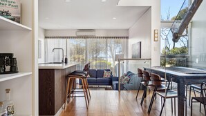 Une cuisine moderne dotée d’un îlot central, d’un coin repas avec des tabourets de bar, d’un canapé et d’une grande fenêtre agrémentée de rideaux.