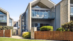 Un immeuble résidentiel moderne à deux étages, doté d’un balcon, de grandes fenêtres et d’un jardin bien entretenu.