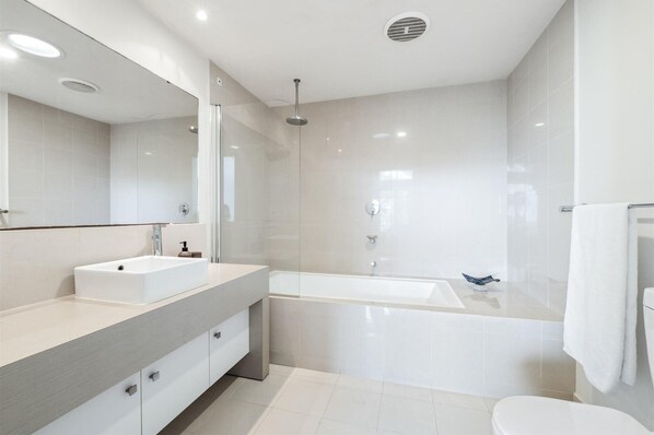 A modern bathroom with a large mirror, two sinks, a bathtub, and a toilet. - Serenity at Seine - Serenity at Seine Bay No.5 (3 Bedroom) (Augusta)