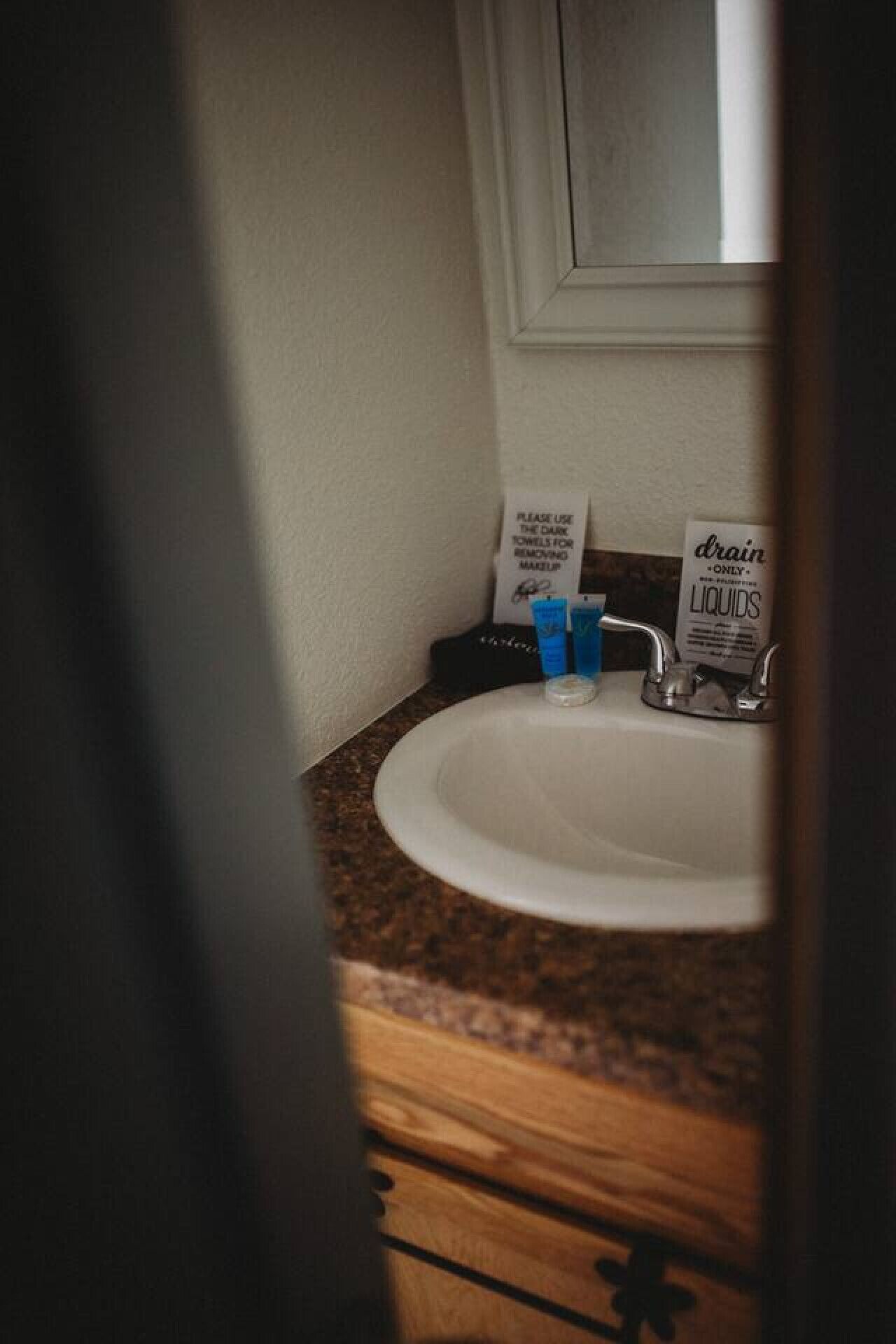 A bathroom sink with a dark towel dispenser, a bottle of drain cleaner, and a blue bottle on the counter.