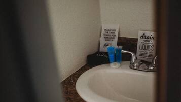A bathroom sink with a dark towel dispenser, a bottle of drain cleaner, and a blue bottle on the counter.