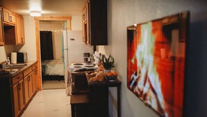 A kitchen with wooden cabinets, a refrigerator, a stove, and a dining table with oranges. - Raven's Perch Cabin B Peaceful Getaway-Aurora-AlaskanCabin (Fairbanks)