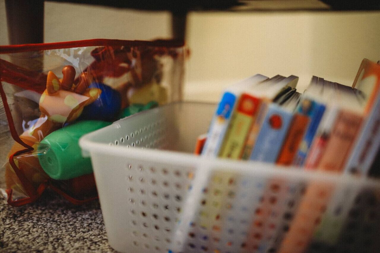 Een mand gevuld met tijdschriften en een doorzichtige plastic tas met een speeltje.