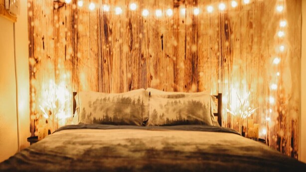 A bed with a wooden headboard and string lights. - Raven's Perch Cabin B Peaceful Getaway-Aurora-AlaskanCabin (Fairbanks)