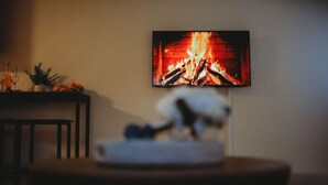 A room with a television displaying a fireplace, a small table with a decorative item, and a chair. - Raven's Perch Cabin B Peaceful Getaway-Aurora-AlaskanCabin (Fairbanks)