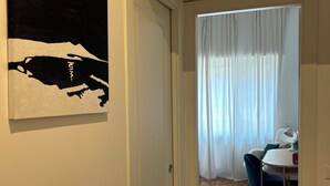 A hallway leading to a dining area with a table and chairs, a white door, and a black and white artwork on the wall. - Roma [appartamento Moderno e Luminoso] (Roma)