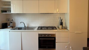 A modern kitchen with white cabinets, a stainless steel sink, a gas stove, and an oven. - Roma [appartamento Moderno e Luminoso] (Roma)