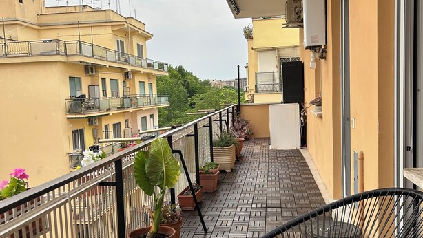 A balcony with potted plants, a black chair, and a tiled floor. - Roma [appartamento Moderno e Luminoso] (Roma)