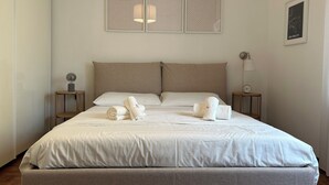 A neatly made bed with white linens and rolled towels, a wooden nightstand with a lamp, and a framed map on the wall. - Roma [appartamento Moderno e Luminoso] (Roma)