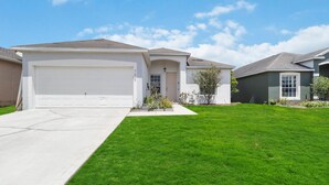 A residential house with a white garage, a well-maintained lawn, and a clear blue sky. - 5/3 Pool home located in Sunset Ridge Community! (Davenport)