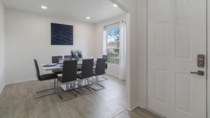 A dining area with a white table, black chairs, and a modern wall art piece. - 5/3 Pool home located in Sunset Ridge Community! (Davenport)