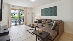 A living room with a brown leather sofa, two black coffee tables, a television, and a view of an outdoor pool area. - 5/3 Pool home located in Sunset Ridge Community! (Davenport)