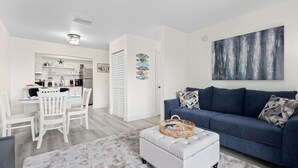 Een moderne woonkamer met een blauwe bank, een witte voetenbankje en een grijs vloerkleed.