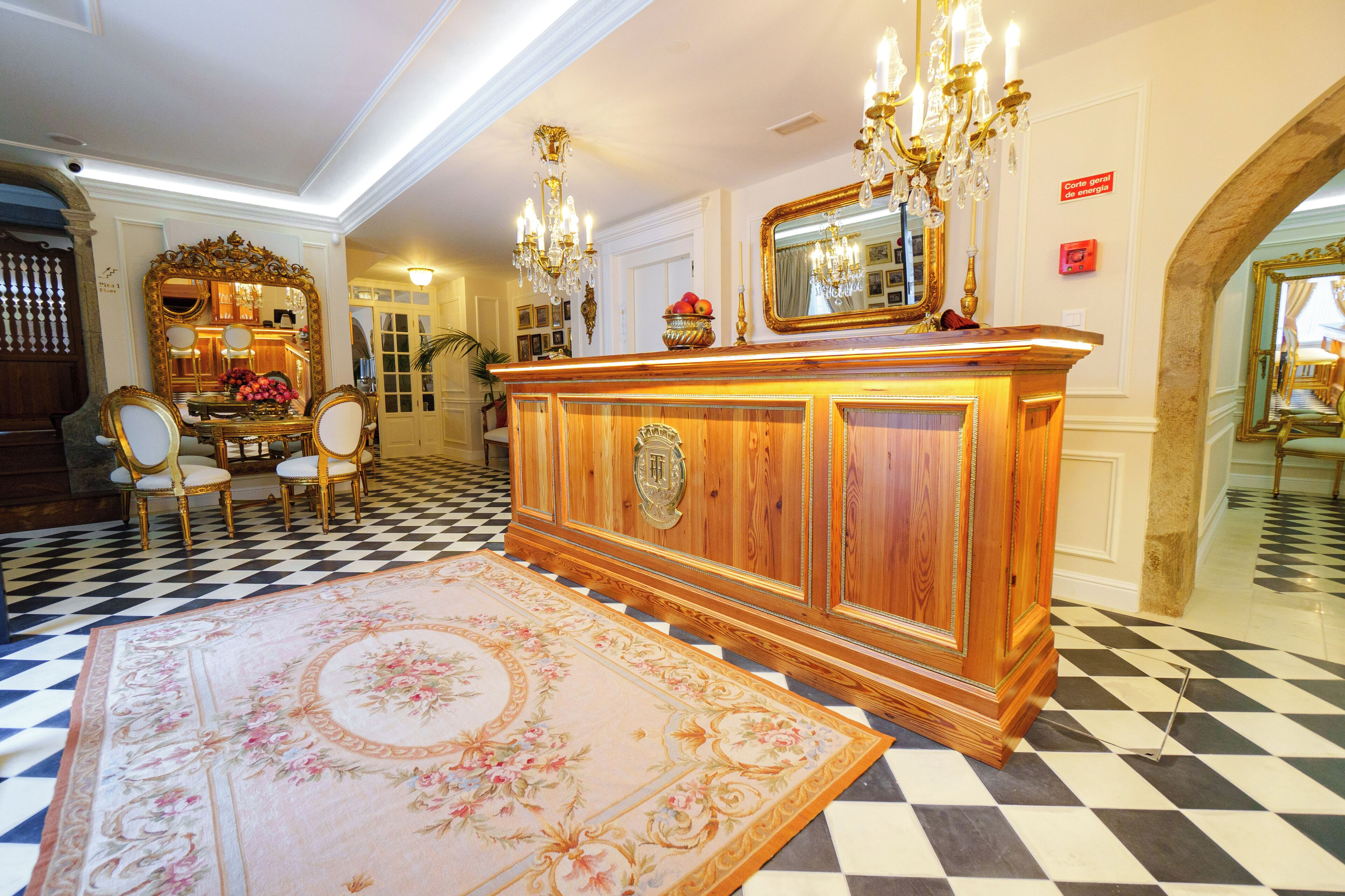 Una sala imponente con piso de tablones de ajedrez, un mueble de madera grande y ornamentado con espejo, y una araña.