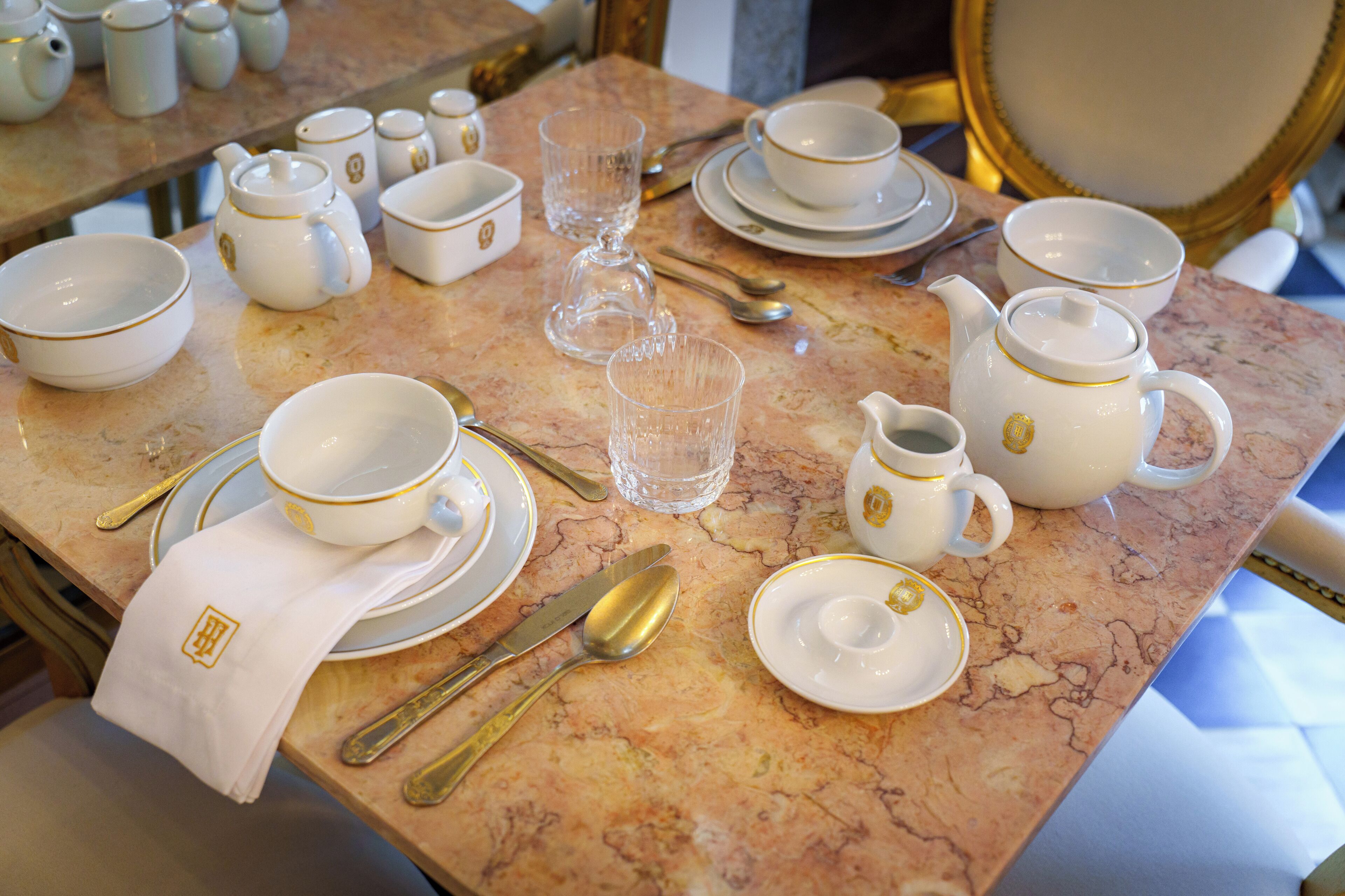 Une table dressée avec de la vaisselle blanche et dorée, comprenant des assiettes, des bols et une théière, posée sur une surface en marbre.