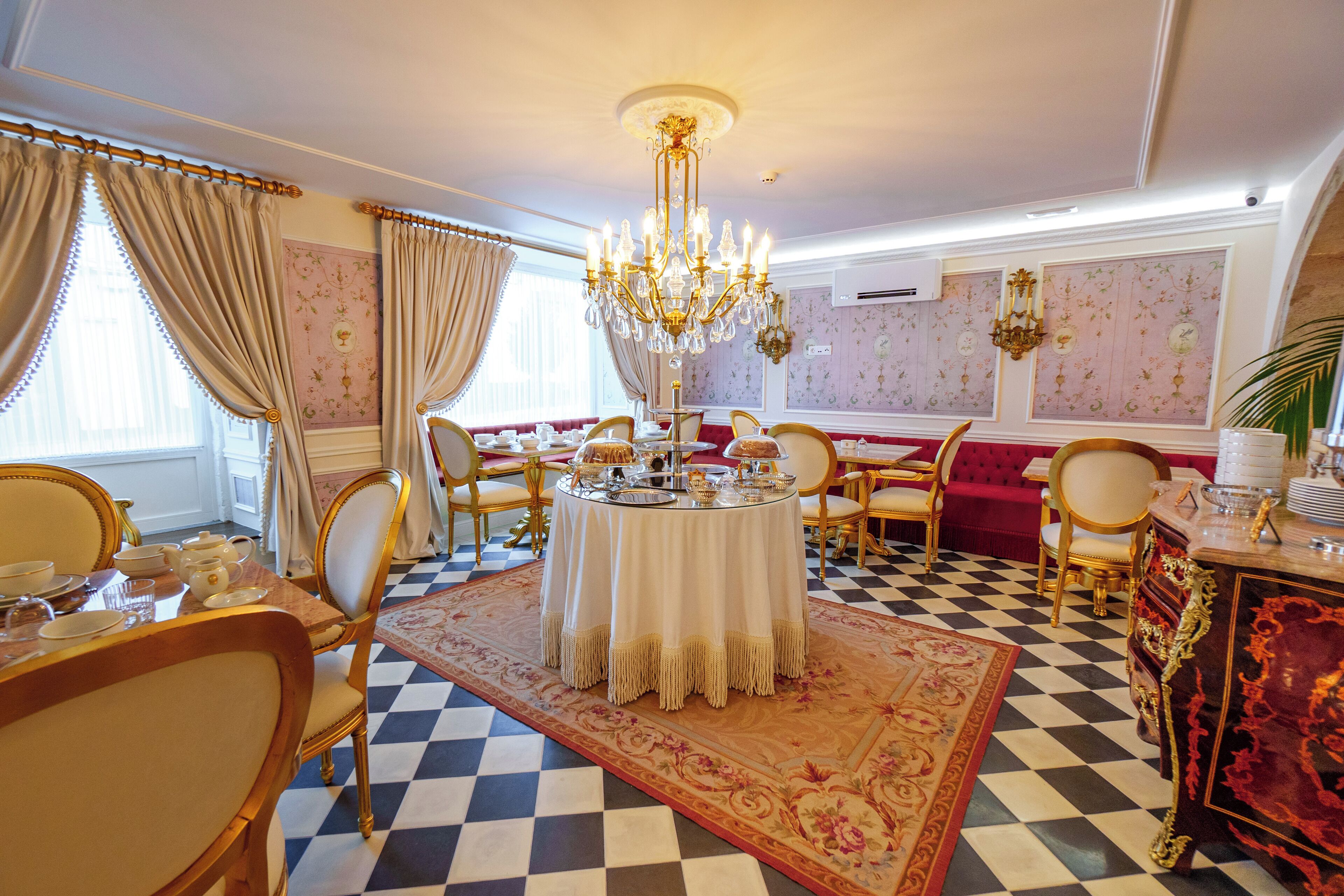 A dining area with a checkered floor, a round table with a white tablecloth, and gold chairs.