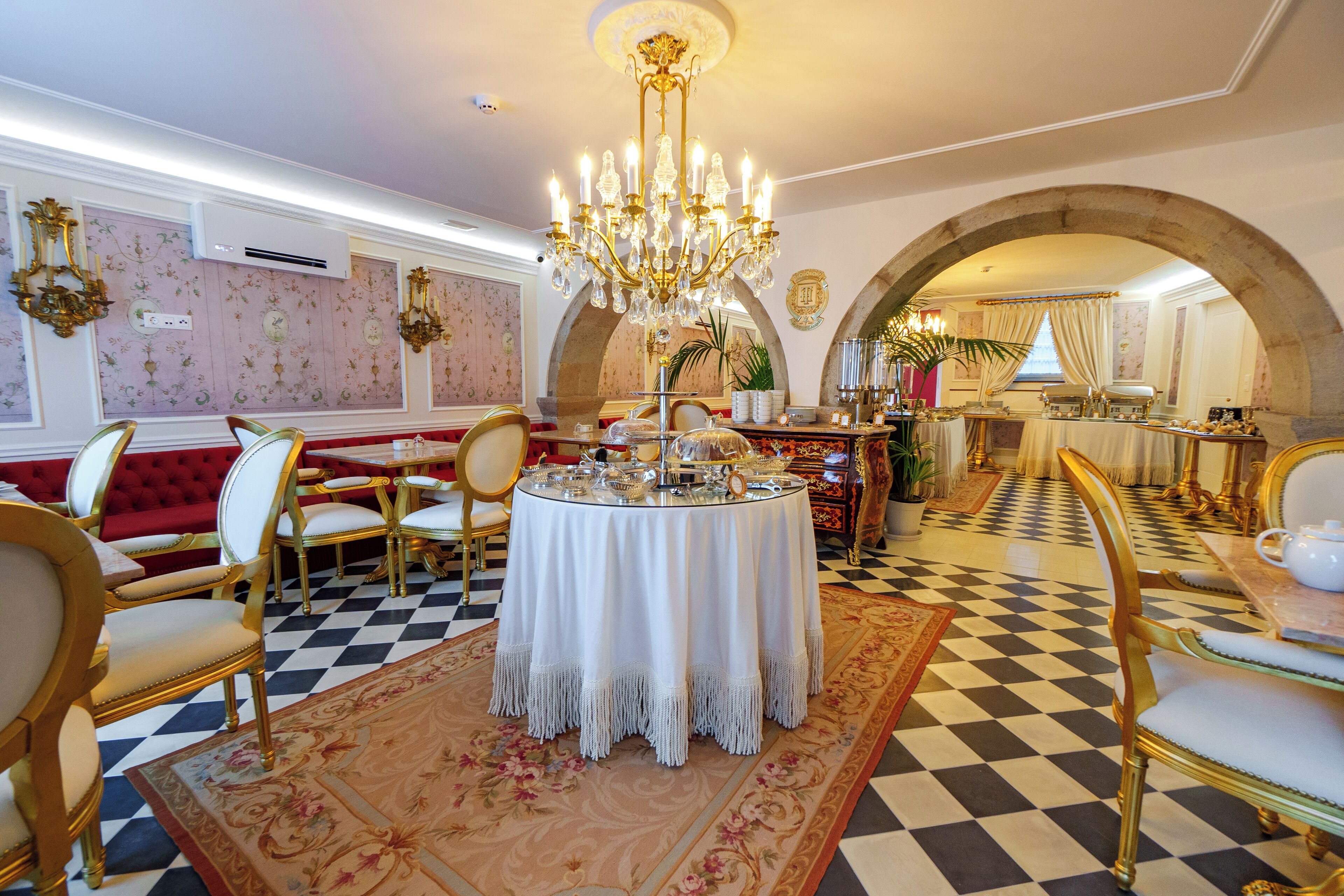 A dining area with a checkered floor, a round table with a white tablecloth, and gold chairs.