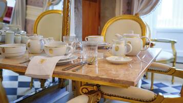 A dining table set with white and gold china, glassware, and silverware, surrounded by ornate chairs.