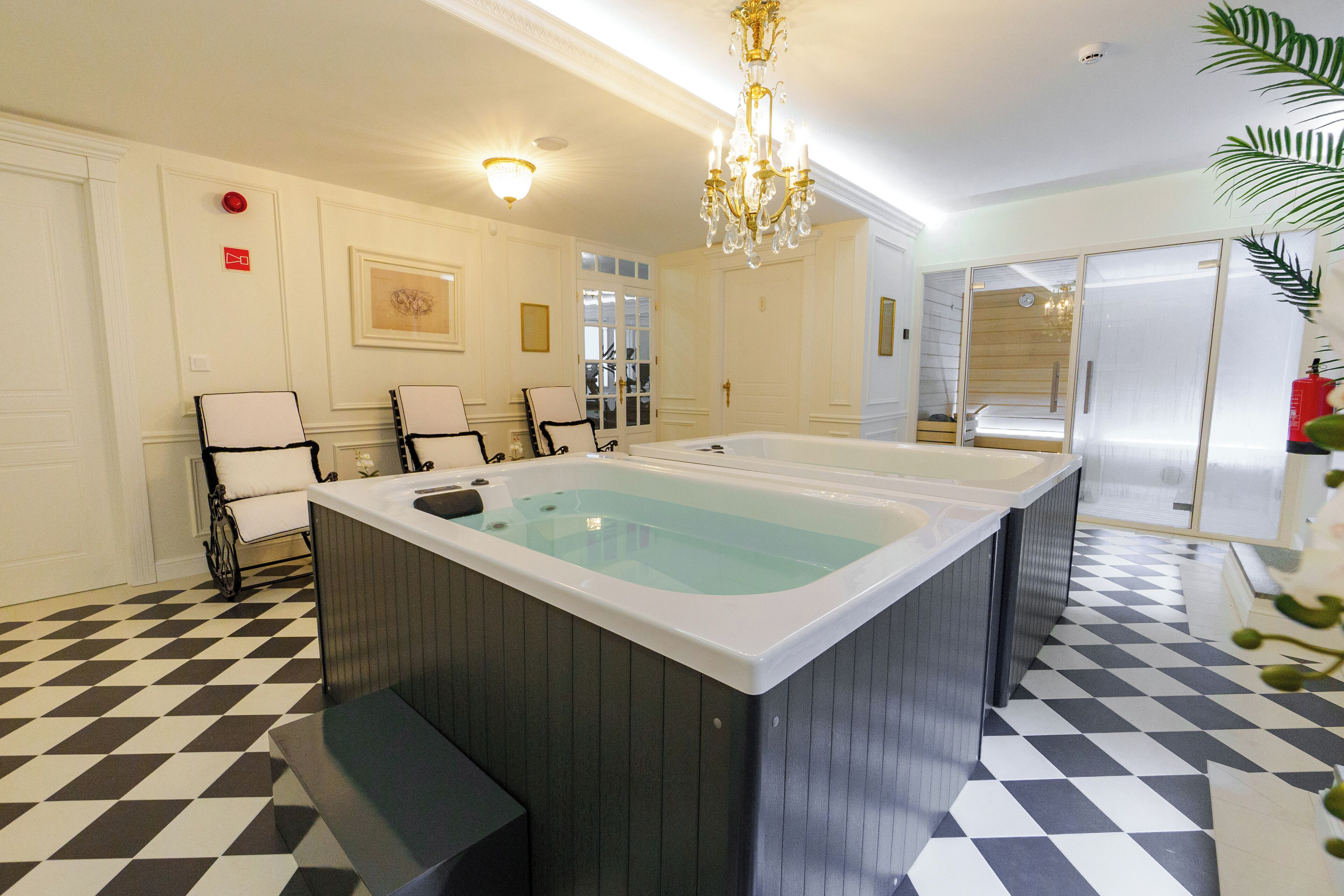 A modern bathroom with a large bathtub, a chandelier, and a checkered floor.