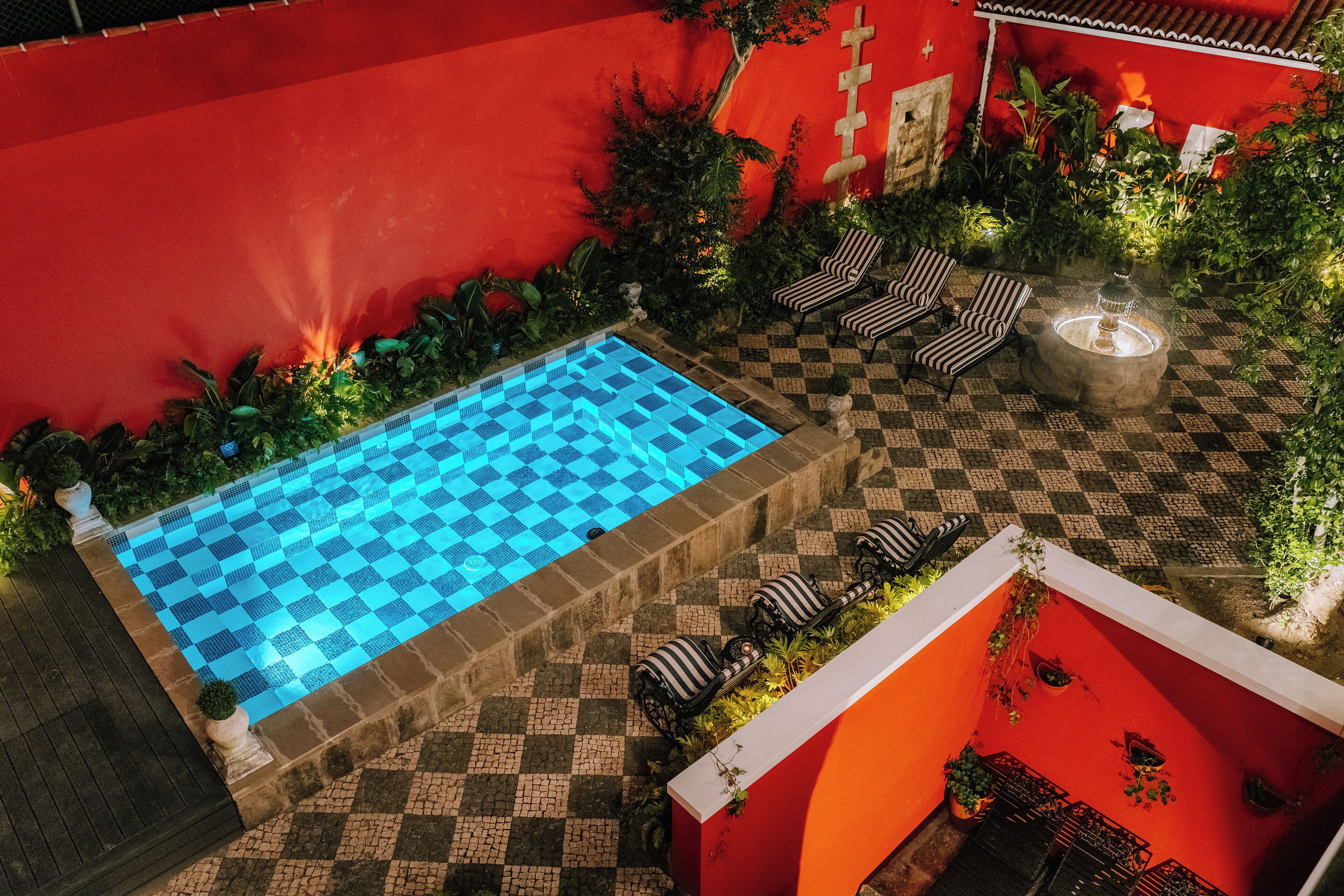 Zona de piscina en la azotea con piscina a cuadros, sillas de descanso y una chimenea.