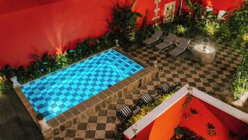 Zona de piscina en la azotea con piscina a cuadros, sillas de descanso y una chimenea.