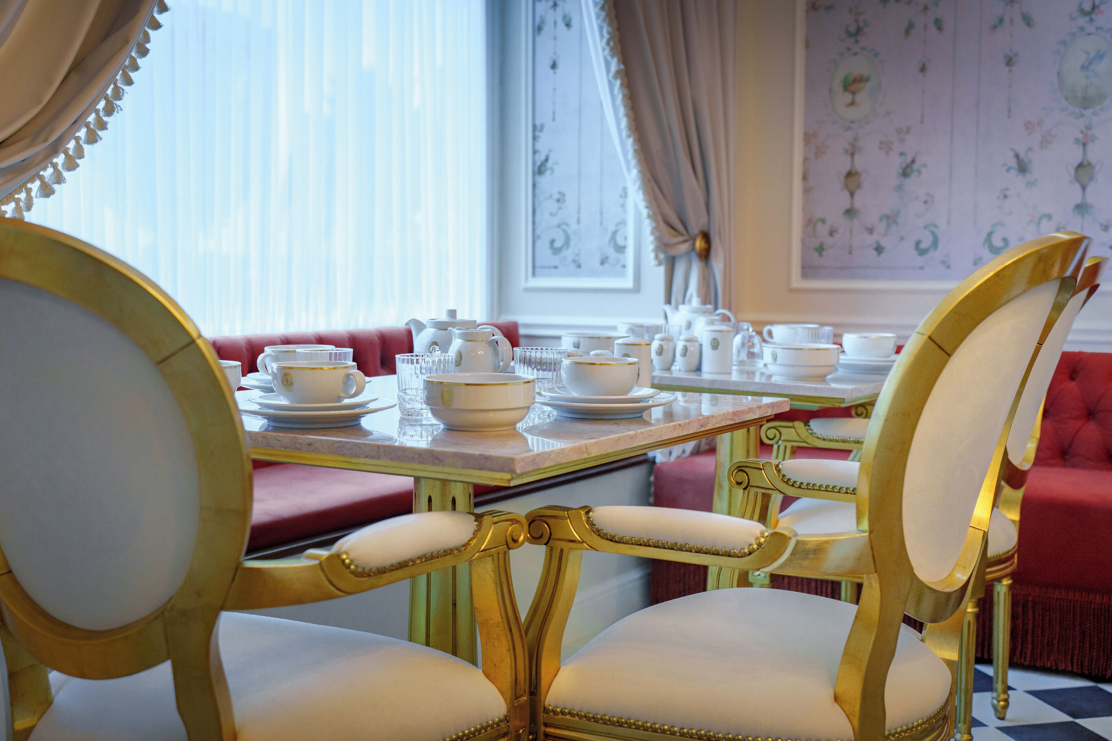A dining area with ornate gold chairs and a table set for tea, featuring white teapots and cups.