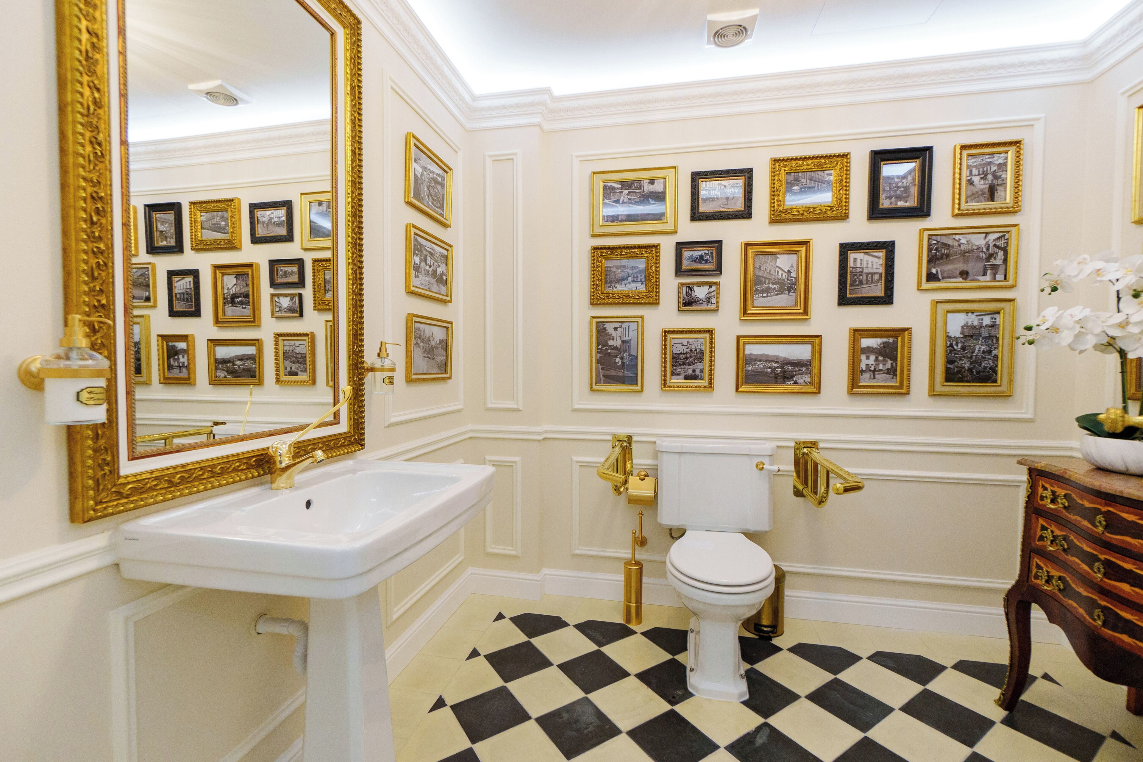 A bathroom with a white sink, gold fixtures, a white toilet, and a checkered floor.