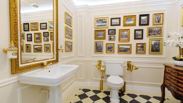 A bathroom with a white sink, gold fixtures, a white toilet, and a checkered floor.