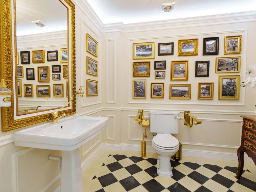 A bathroom with a white sink, gold fixtures, a white toilet, and a checkered floor.