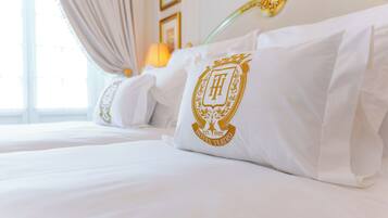 A neatly made bed with white linens and a pillow featuring a gold emblem.
