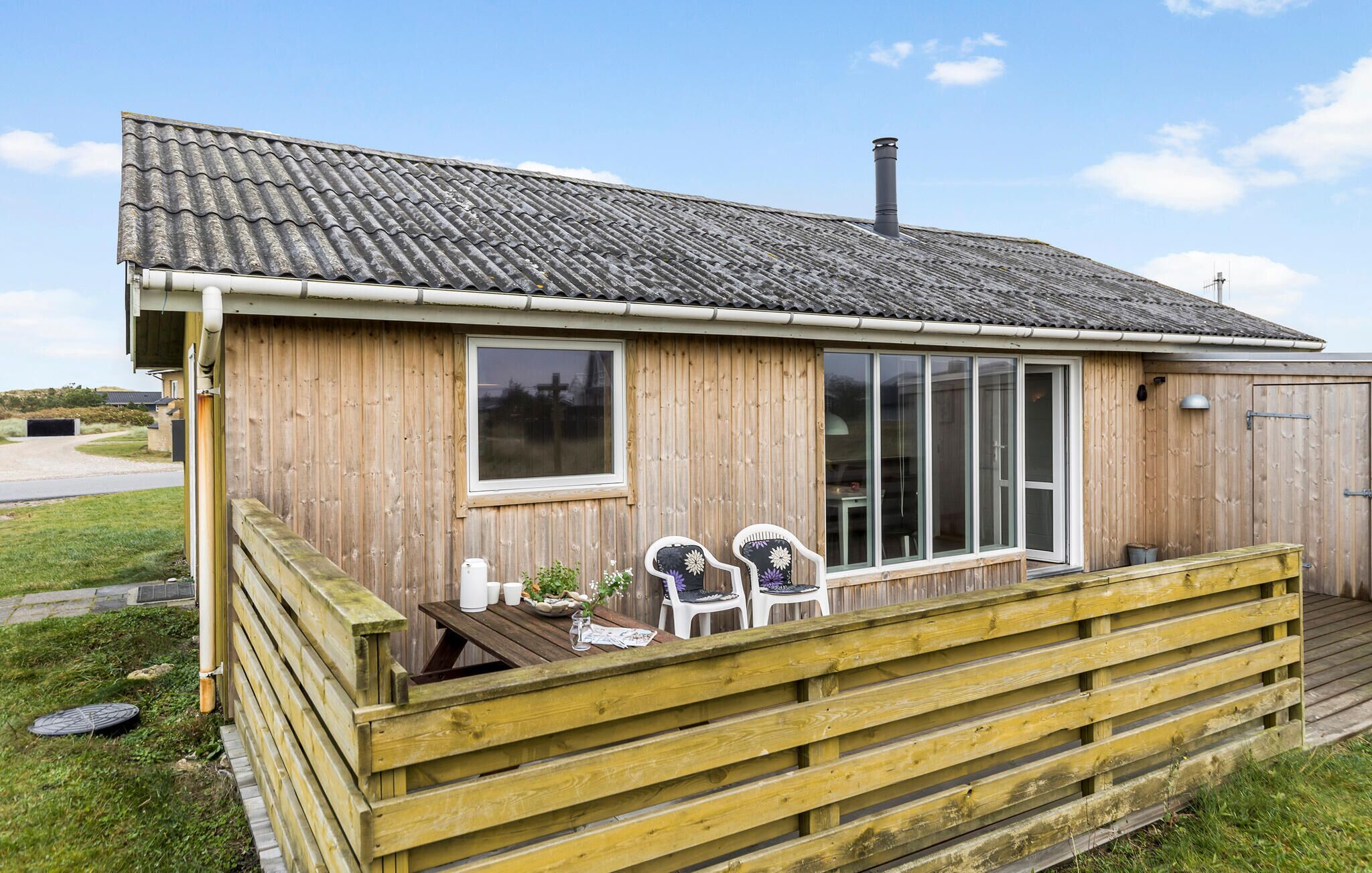 En stuga byggd av trä med ett tak täckt av takpannor, en veranda med ett bord och stolar samt en stor skjutdörr av glas.