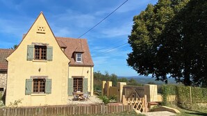 A two-story house with a sloped roof and green shutters, surrounded by a wooden fence and a grassy yard. - "Sur la colline": country house with heated pool, near Sarlat. (Domme)
