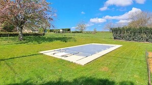 A grassy outdoor area with a rectangular concrete structure, possibly a pool or patio, surrounded by trees and a hedge. - "Sur la colline": country house with heated pool, near Sarlat. (Domme)