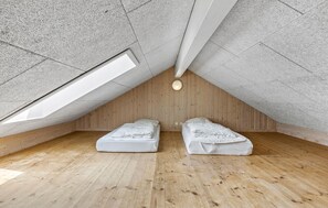 Un pequeño dormitorio en el ático con dos camas, piso de madera y techo inclinado con tragaluces.