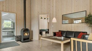 Ett mysigt vardagsrum med en öppen spis, träpanel på väggarna, ett biljardbord och en soffa.
