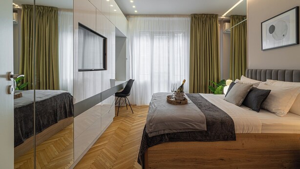 A modern bedroom with a bed, bedside table, and a chair. There is a window with curtains, a mirror, and a framed picture on the wall. - Urban 1BR Loft Residences - Modern Comfort in Bucharest Center (Bucharest)