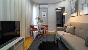 A modern living room with a sofa, TV, and a dining area with chairs and a table. - Urban 1BR Loft Residences - Modern Comfort in Bucharest Center (Bucharest)