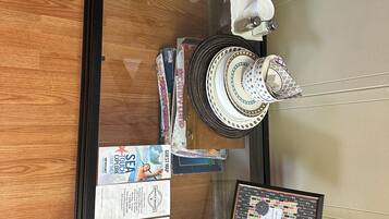 A glass-top table with a black metal frame, a woven basket, a glass bottle, a stack of plates, a set of cutlery, and a menu.