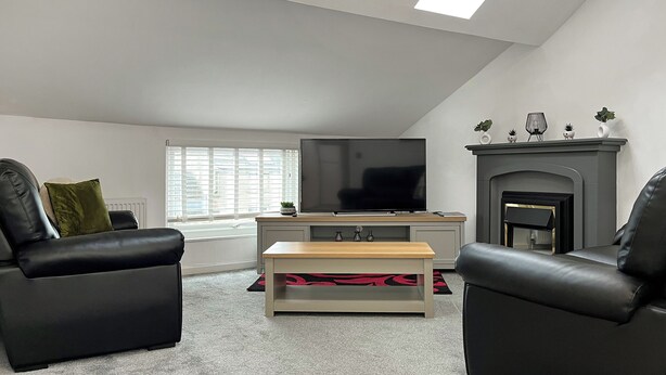 A modern living room with a flat-screen TV, two leather sofas, a coffee table, and a fireplace.