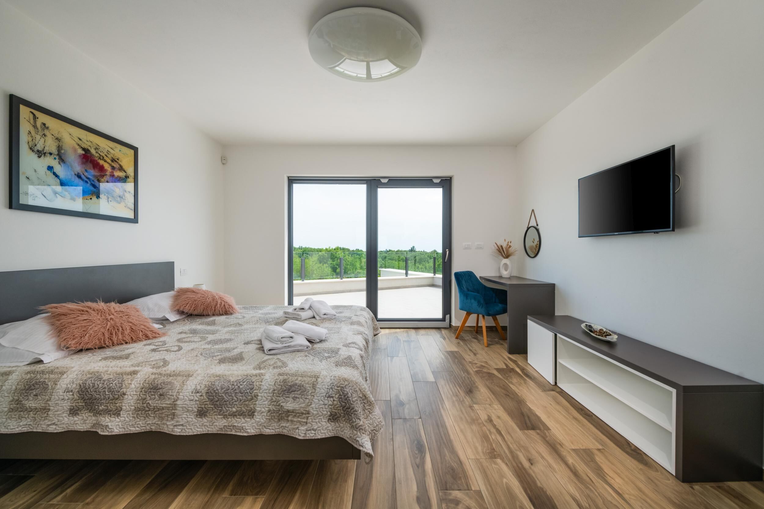 A modern bedroom with a large bed, a desk, a chair, and a TV.