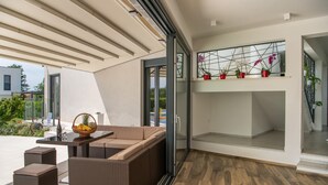 Une terrasse extérieure moderne, dotée d’une porte vitrée donnant sur un balcon, de meubles en osier et d’une petite table sur laquelle se trouve un panier de fruits.