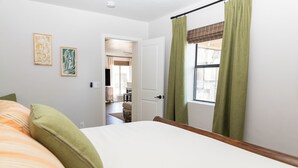 Un dormitorio con cama, cortinas verdes y dos cuadros enmarcados en la pared.