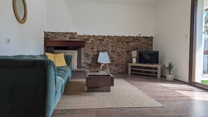 A living room with a stone wall, a green sofa, a coffee table, a TV, and a potted plant. - Spacious Holiday Home 10 Minutes from the Stunning Beaches of Western Sardinia (Donigala Fenughedu)
