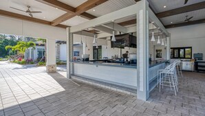 An outdoor bar area with a counter, ceiling fans, hanging pendant lights, and a view of the outdoors. - Modern Clean Design Near Disney Top Resort (Kissimmee)