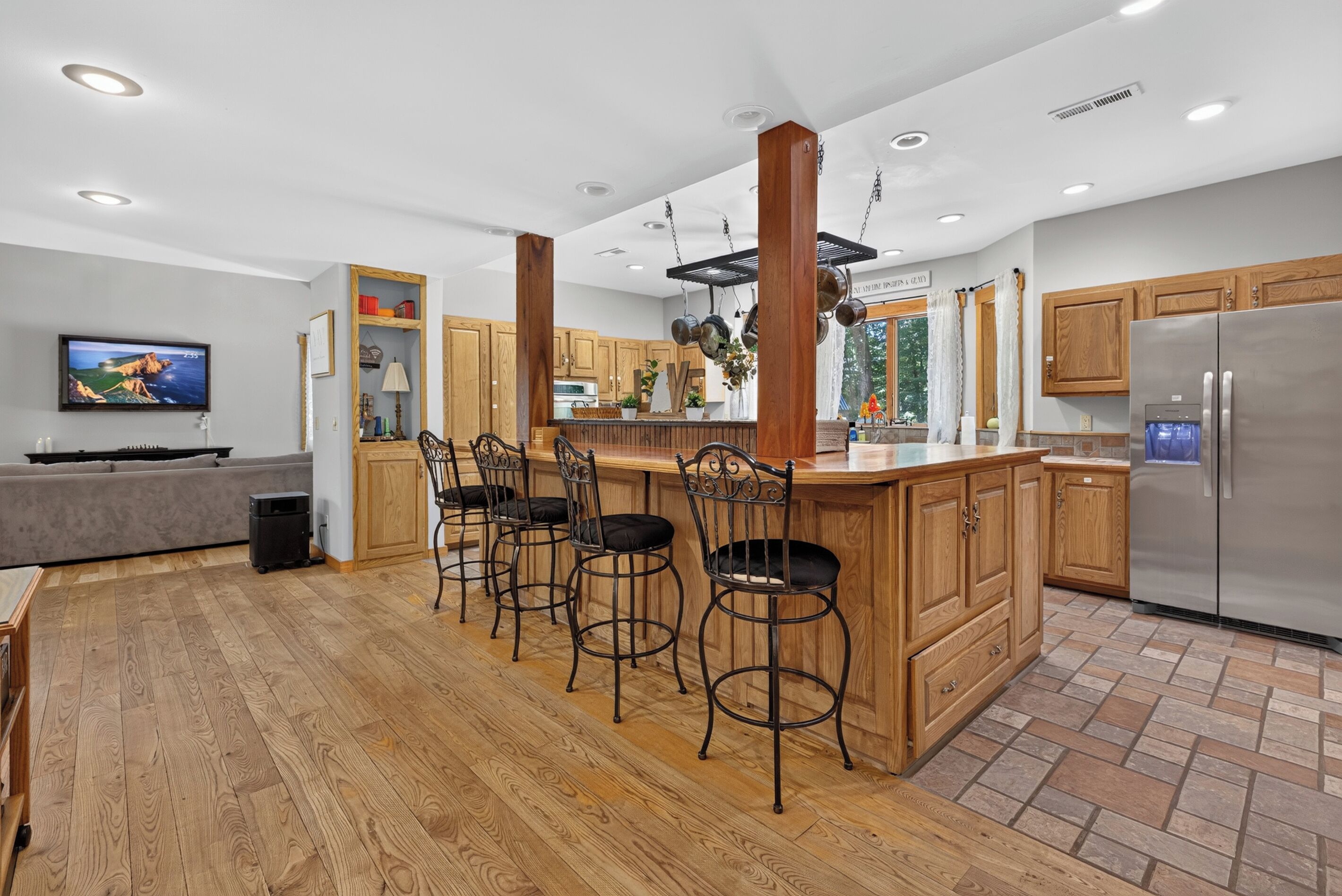 A modern kitchen with wooden cabinets, a stainless steel refrigerator, and a bar area with stools.