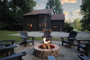 A fire pit with chairs around it, a house in the background, and a gravel area. - Story Time Retreat (Nashville)