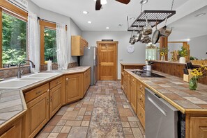 A modern kitchen with wooden cabinets, a stainless steel dishwasher, and a large window with curtains. - Story Time Retreat (Nashville)