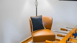 Une pièce avec un fauteuil en cuir marron, un coussin foncé, un plancher en bois et une table de baby-foot.
